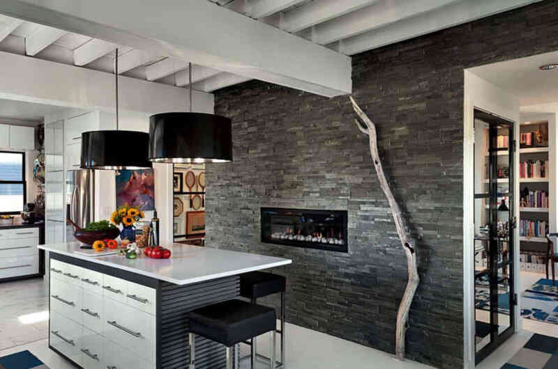 Yenilenmiş sahil evinde modern tarzda bir mutfak, yığma taş duvarda yine modern tarzda mutfakla iyi entegre olmuş bir şömine.