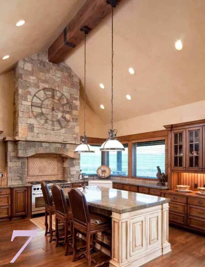 Büyük dekoratif saat, pişirme alanının büyük taş rafını tamamlıyor. Bu, havalandırma başlığı, ortada tek bir açık ahşap kirişin bulunduğu bej katedral tavana kadar uzanıyor.