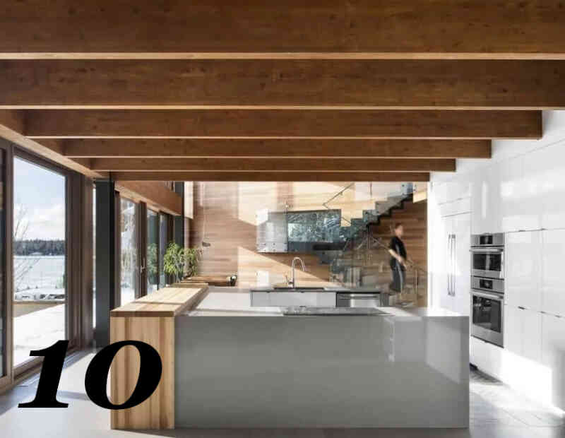 Şık ve pürüzsüz beyaz yüzeylere sahip dolaplarla ortada U şeklinde büyük bir mutfak adasına sahip modern mutfak tasarımı. Büyük cam sürgülü kapılar ve düz geniş ahşap kirişlere sahip modern tavan tasarımı.